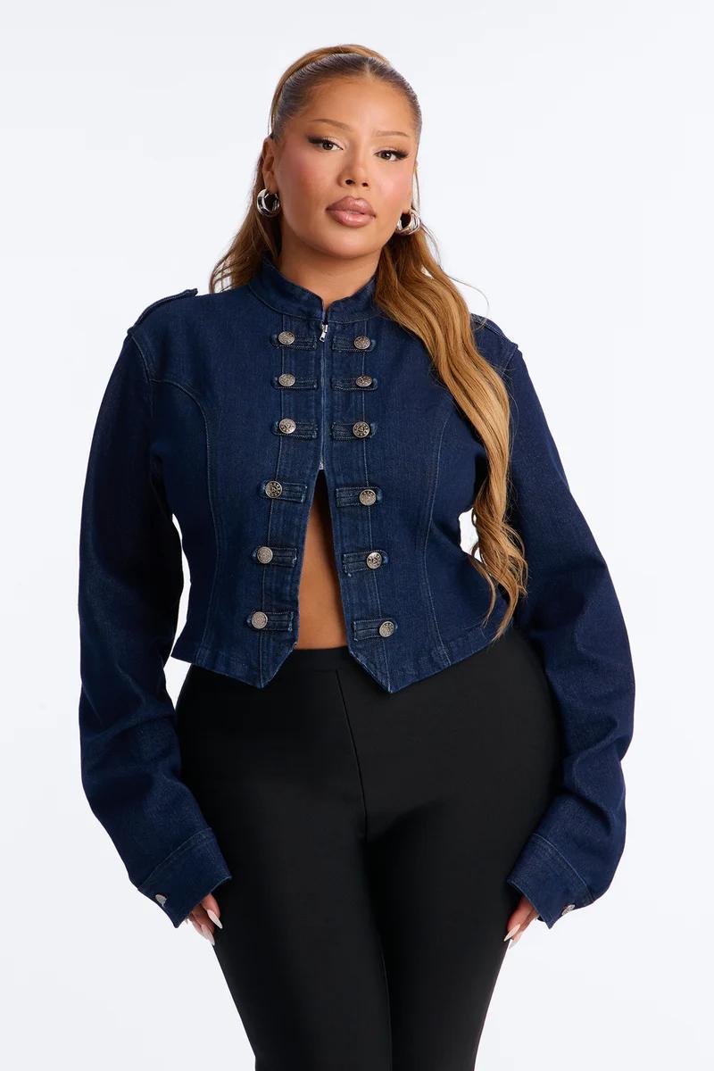 Plus size woman wearing a cropped dark wash military denim jacket with silver buttons.