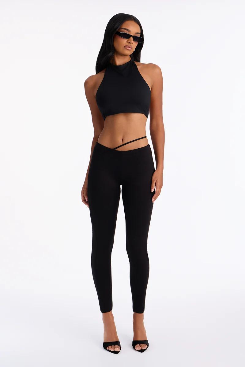 Woman wearing a black halter crop top and matching strappy low-rise leggings.