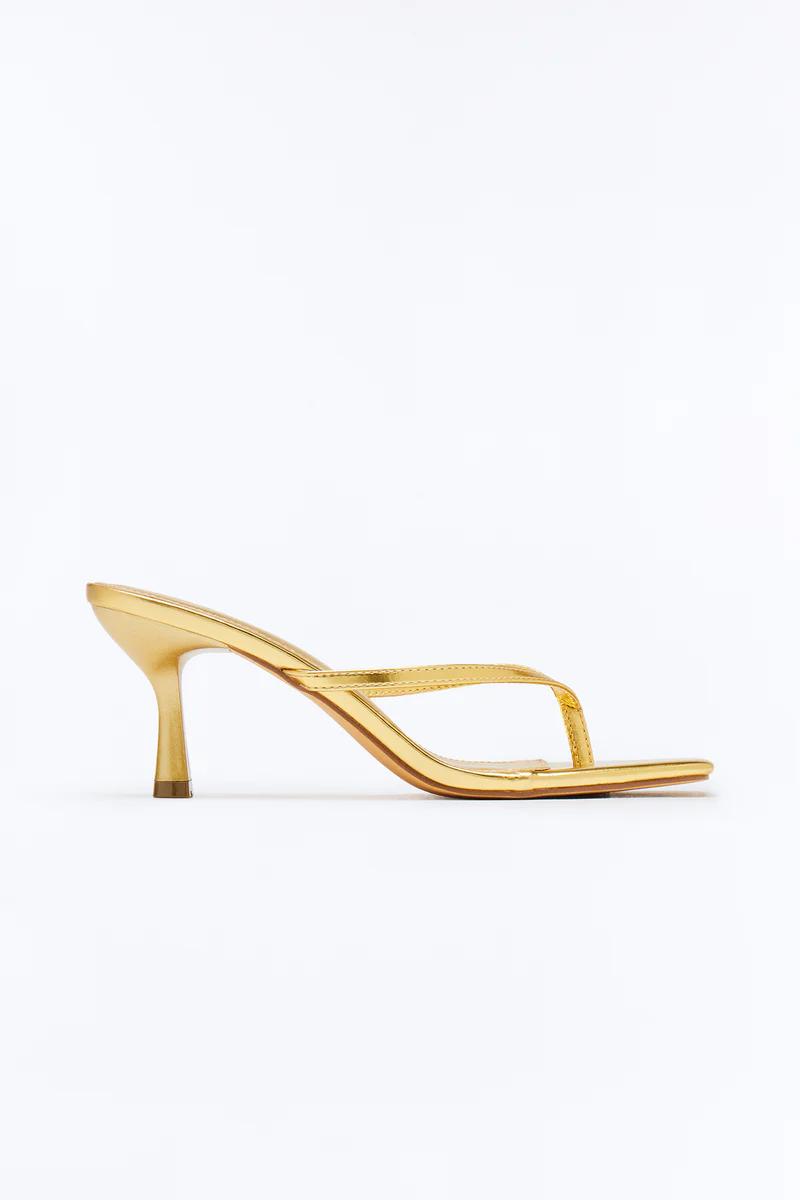 Single metallic gold high-heeled thong sandal with a square toe and flared heel, viewed from the side on a white background.