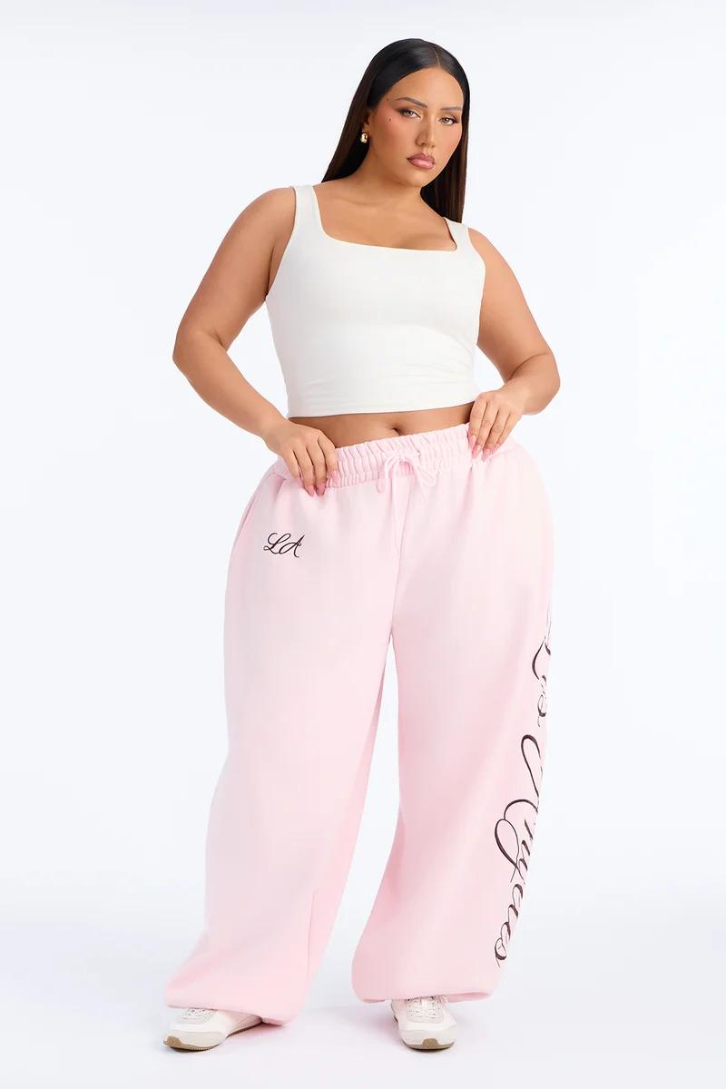 Plus size woman wearing a white square-neck crop top and light pink baggy LA sweatpants.
