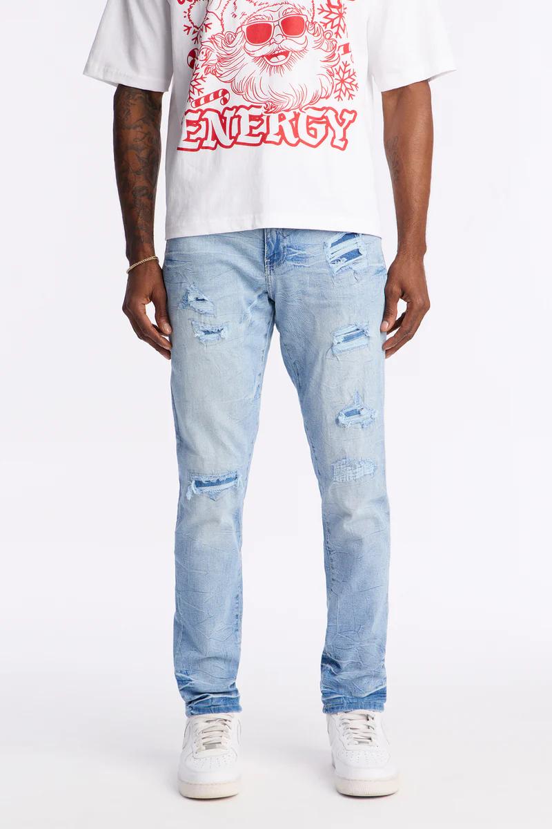 Hombre luce camiseta gráfica blanca "ENERGY" y vaqueros denim azules claros con rotos y parches, zapatillas blancas. Explora moda masculina.