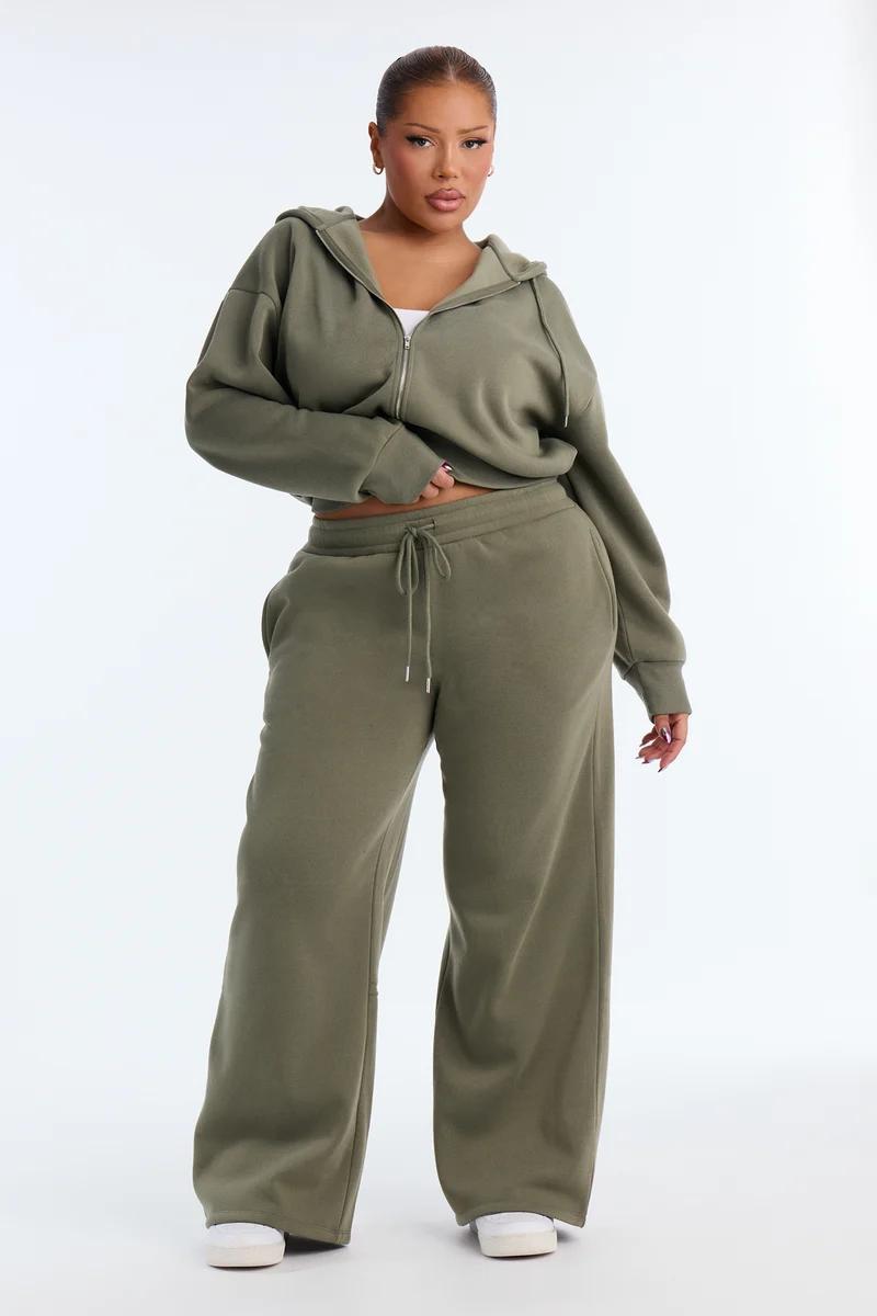 Plus-size woman wearing an olive green zip-up hoodie and wide-leg sweatpants tracksuit set.
