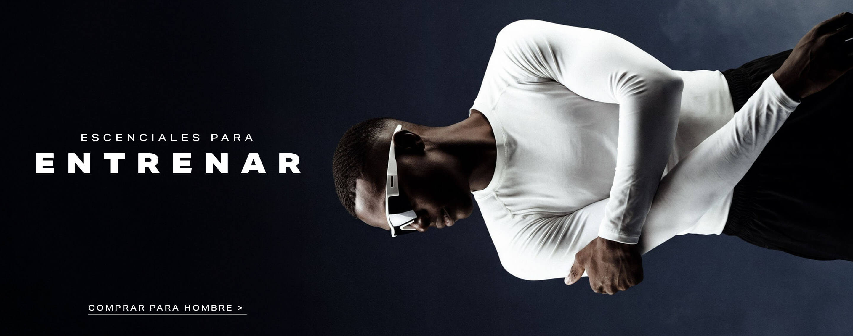 Hombre con camiseta de compresión blanca y gafas deportivas, brazos cruzados. Promueve esenciales de entrenamiento y ropa masculina.
