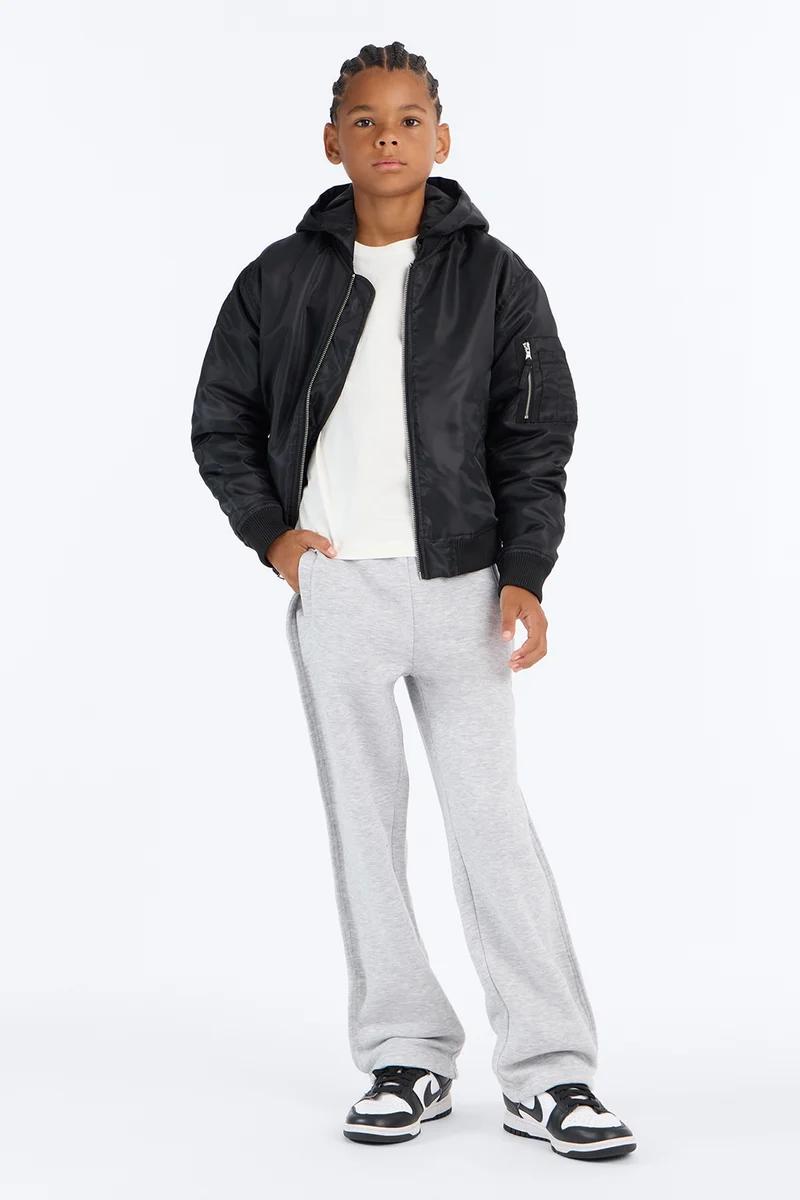 Young boy wearing a black hooded bomber jacket, white t-shirt, grey sweatpants, and black sneakers.