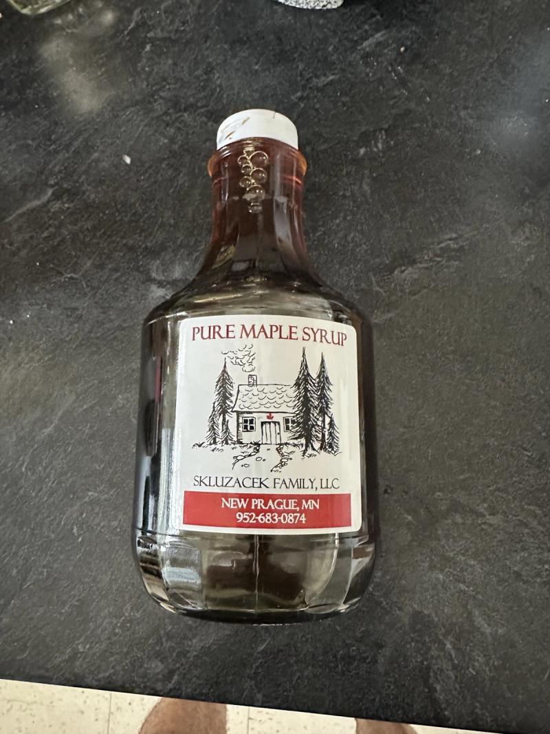A glass bottle of Skluzacek Family pure maple syrup on a dark stone counter