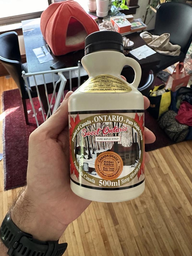 A hand holding a cream-colored 500ml jug of Sweet Ontario pure maple syrup