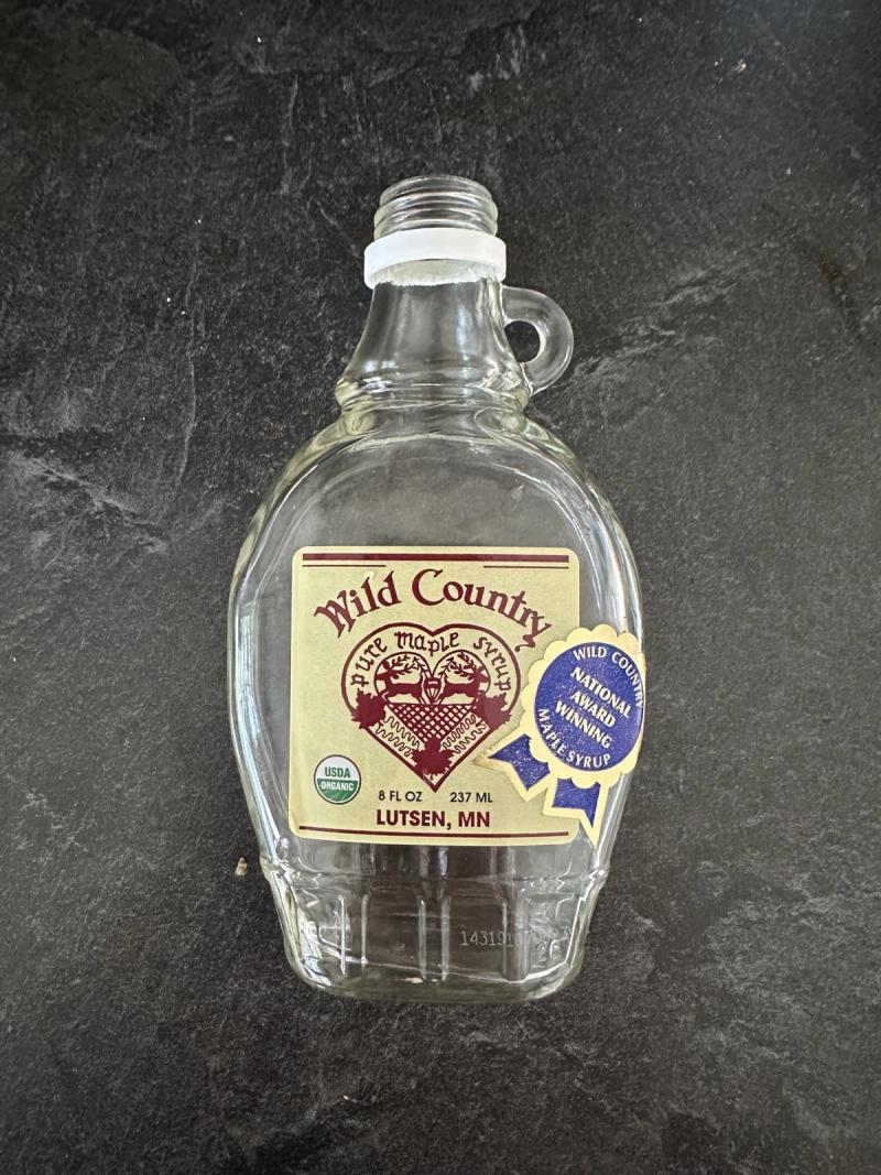An empty 8oz glass bottle of Wild Country organic pure maple syrup