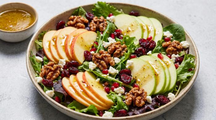 A vibrant green salad topped with red apple slices, cranberries, and candied walnuts in a large serving bowl.
