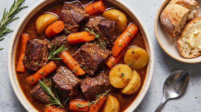 A bowl of rich beef stew with tender chunks of meat and vegetables over creamy mashed potatoes