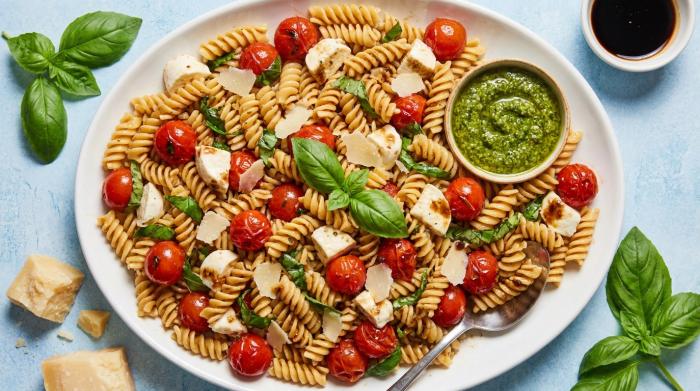 A large serving bowl filled with bruschetta pasta salad topped with fresh basil