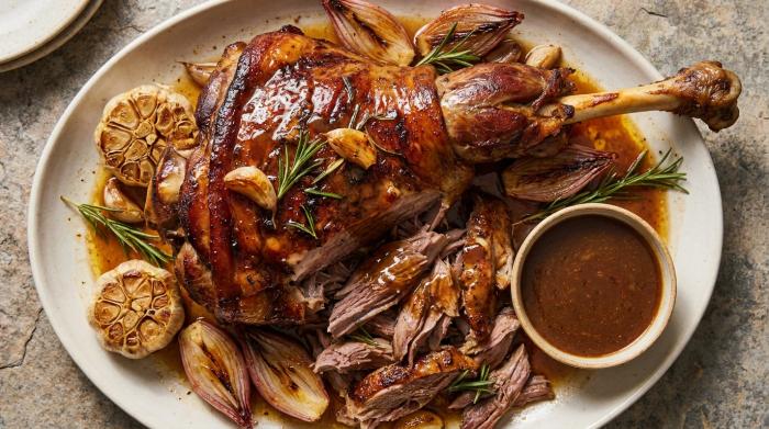 A whole slow-roasted lamb shoulder on a wooden carving board.