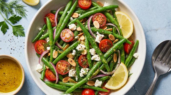 A vibrant green bean salad topped with diced tomatoes, red onions, and a lemon mustard dressing.