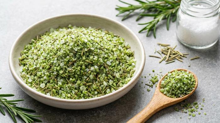 A bowl of bright green rosemary salt next to fresh rosemary.