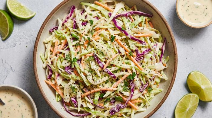 A large serving bowl filled with creamy, fresh coleslaw made of shredded green cabbage and carrots.