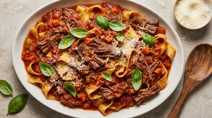 A fork lifting a wide ribbon of pasta coated in a thick, rich shredded beef sauce.