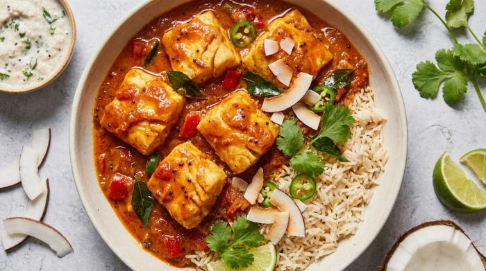 A serving bowl filled with red Goan fish curry and fresh garnishes.