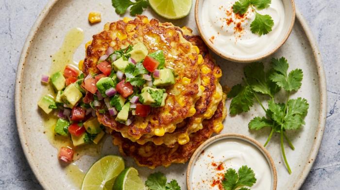Golden brown corn fritters stacked on a plate and topped with chunky avocado salsa.