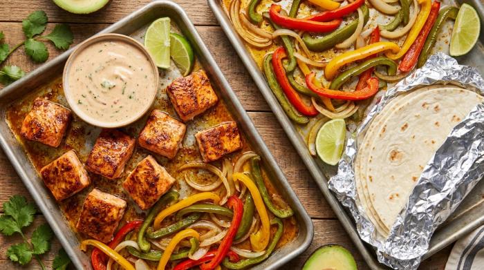 A vibrant spread of baked salmon fajitas with colorful vegetables and toppings on a table.