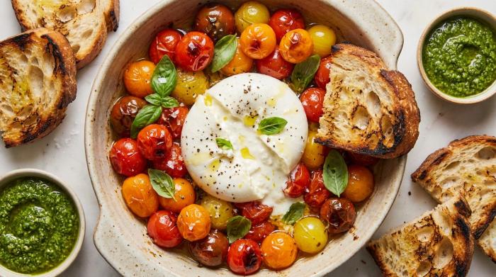 Close-up of creamy burrata center oozing over roasted cherry tomatoes and pesto.