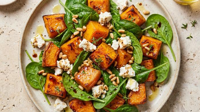 A colorful bowl of roast pumpkin, baby spinach, and feta salad ready to be served.