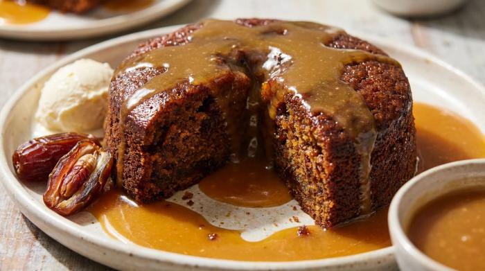 A thick slice of dark sticky date pudding smothered in butterscotch sauce with vanilla ice cream