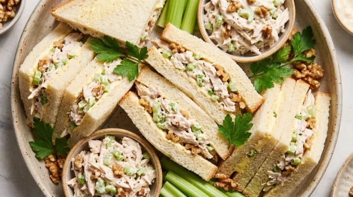A large serving platter piled with crustless chicken sandwiches cut into triangles.