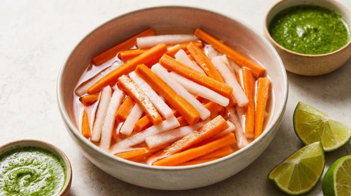 A glass jar filled with pickled carrots and daikon radish in clear liquid.