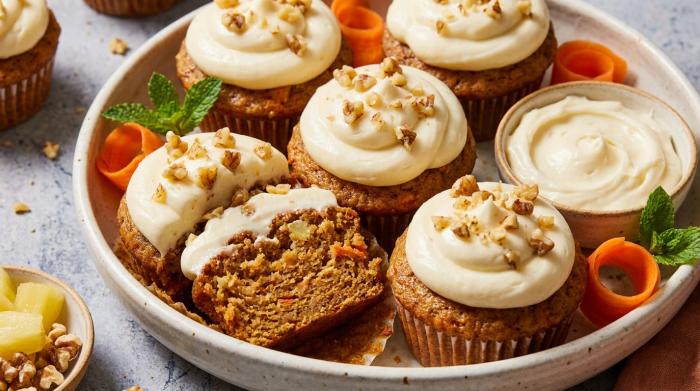 A heavily frosted carrot cake cupcake sprinkled with chopped pecans.