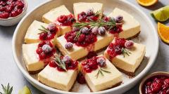 A large rectangular no-bake cheesecake topped with whipped cream, berries, and rosemary.
