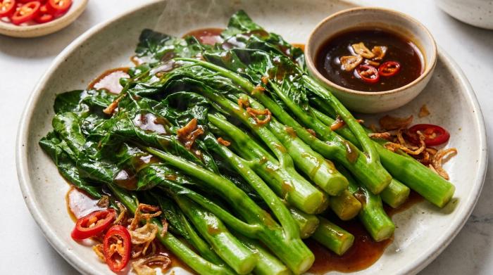 Steamed Chinese broccoli drizzled with garlic ginger oyster sauce on a serving plate.