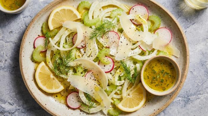 Thinly sliced fennel salad flat on a plate with cheese and dressing.