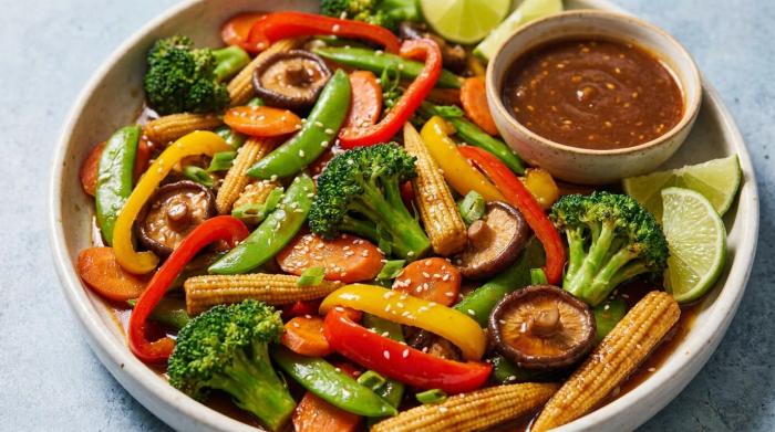 A bowl of glossy vegetable stir-fry served over steaming white rice.