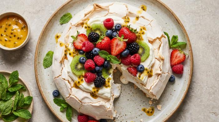 A fully decorated pavlova with a high pile of whipped cream and fresh fruit.