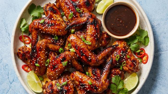 A plate of deeply golden, sticky Chinese chicken wings topped with sesame seeds and green onions.