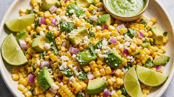 A large bowl filled with vibrant corn salad featuring diced avocado and tomatoes.