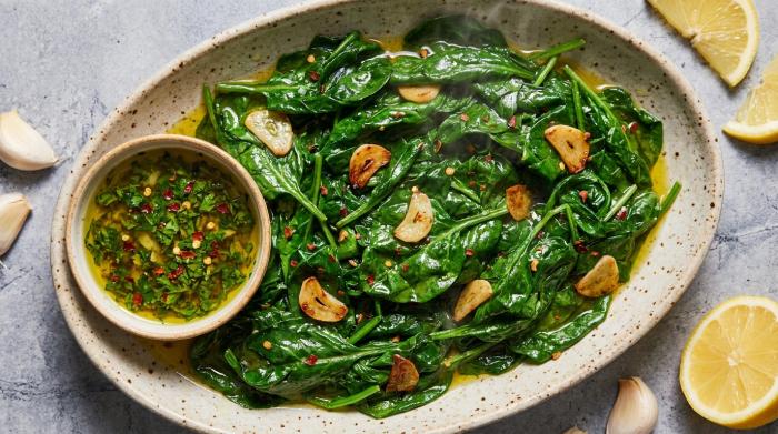 A close-up view of bright green sautéed spinach with specks of cooked garlic in a serving bowl.