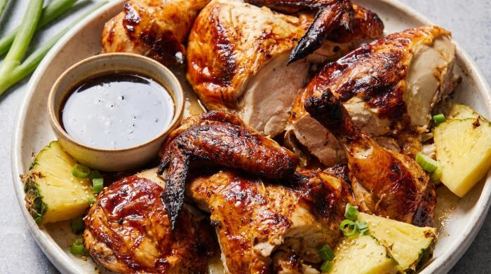 Glazed Huli Huli chicken thighs served with grilled pineapple slices on a platter.