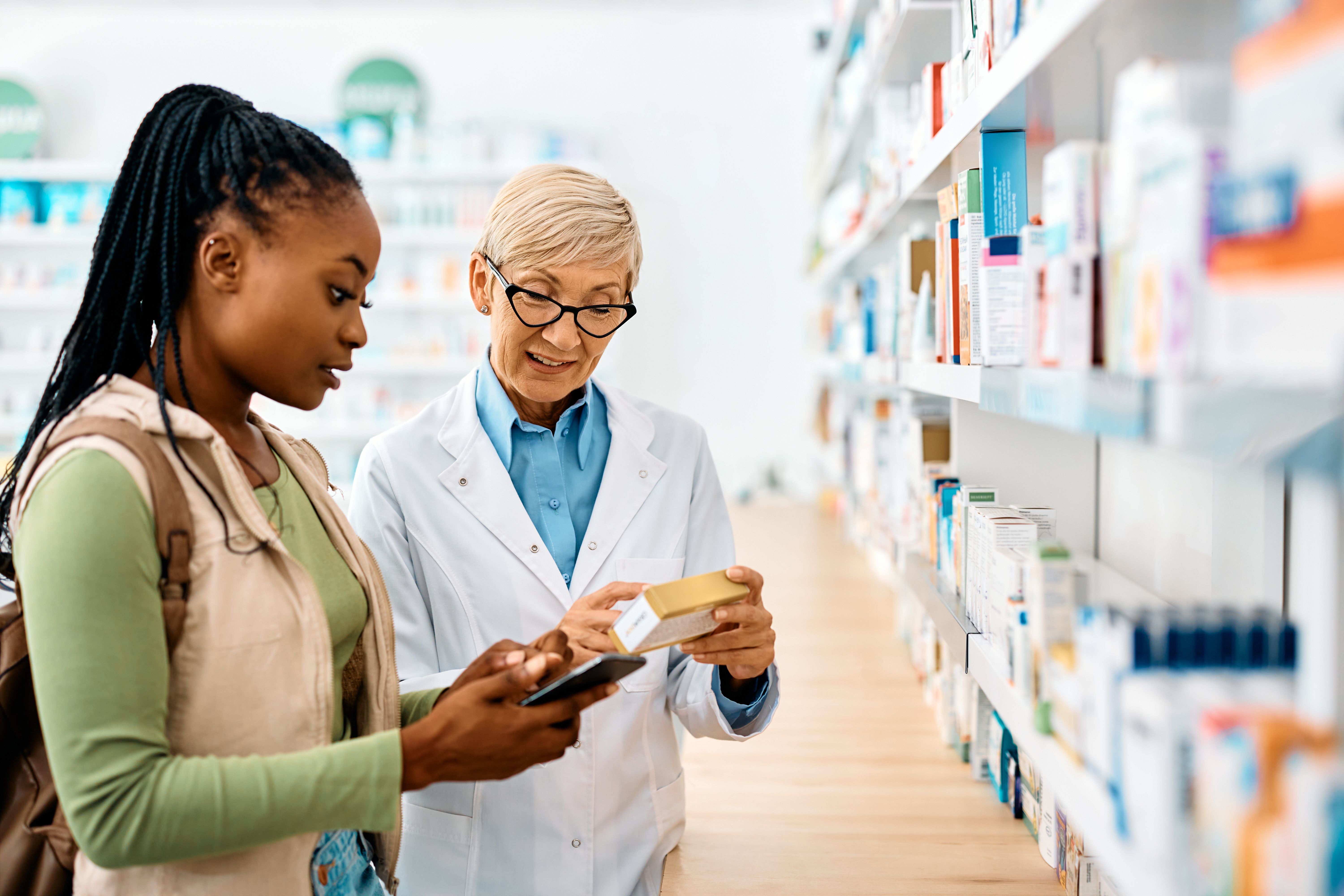 Young black woman gets advice from senior pharmacist while buying medicine in drugstore - Drazen - stock.adobe.com