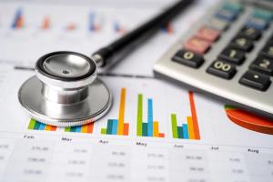 Stethoscope and US dollar banknotes on chart or graph paper| Image Credit: © amazing studio - stock.adobe.com