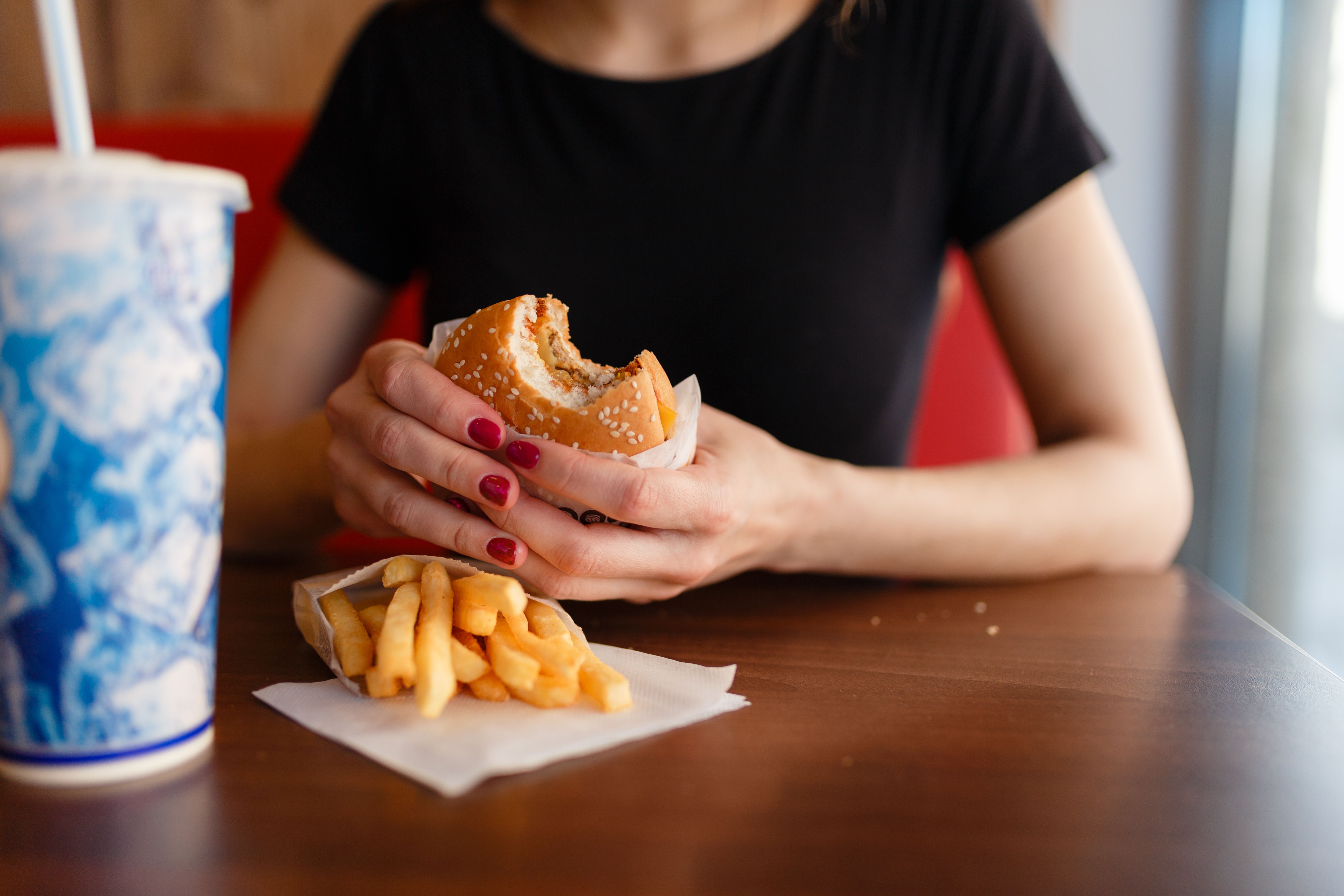 Woman eating burger, fries, and drink | Image credit: korchemkin – stock.adobe.com