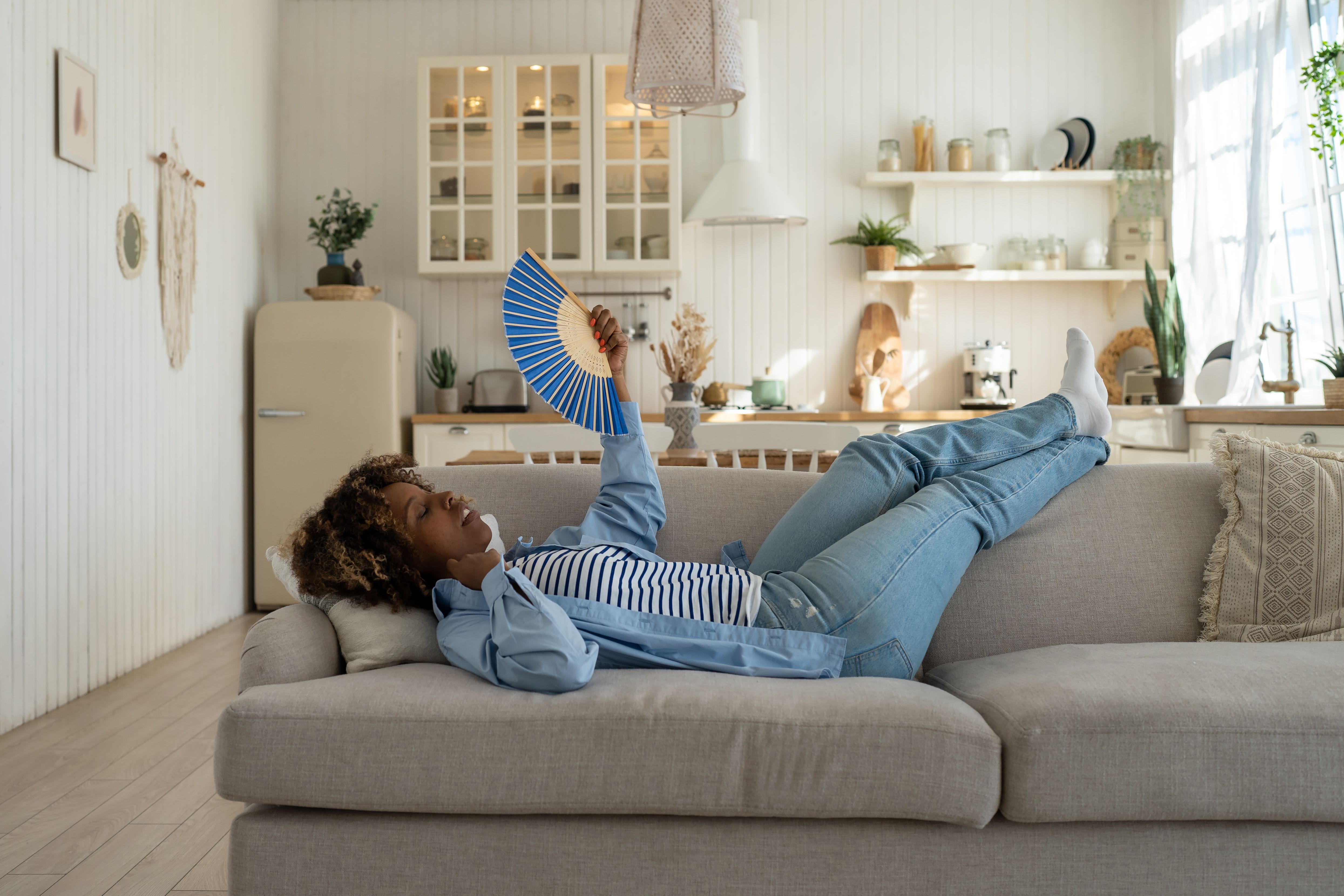 Woman lying on couch having hot flash, fanning herself | Image credit: DimaBerlin – stock.adobe.com