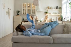 Woman lying on couch having hot flash, fanning herself | Image credit: DimaBerlin – stock.adobe.com