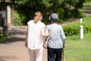 Older adult with cane walking with younger adult in park | Image credit: Masakazu Tokashiki – stock.adobe.com