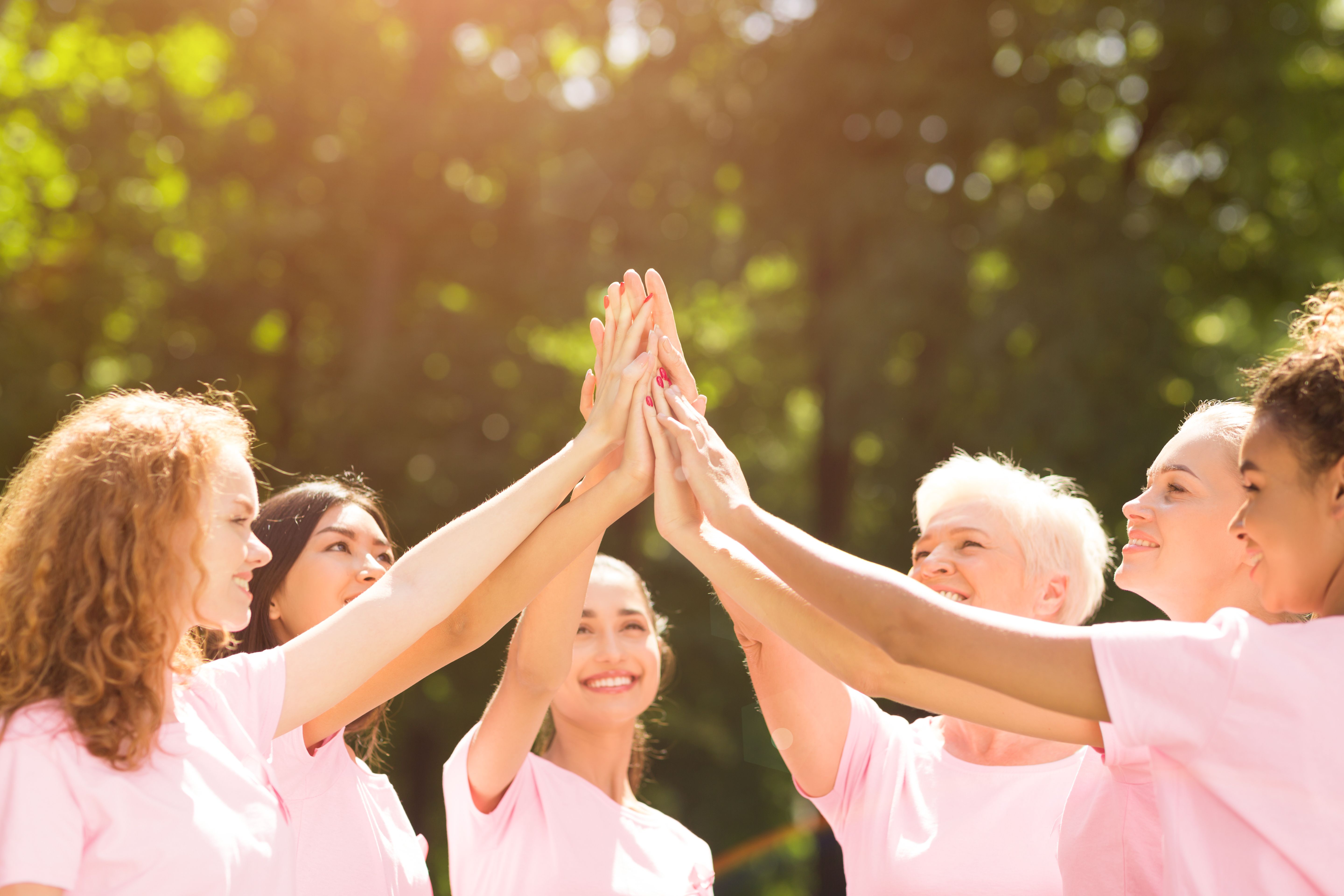 Group of diverse women with pink shirts high-fiving in a circle | Image Credit @Prostock-studio-adobestock_.jpeg