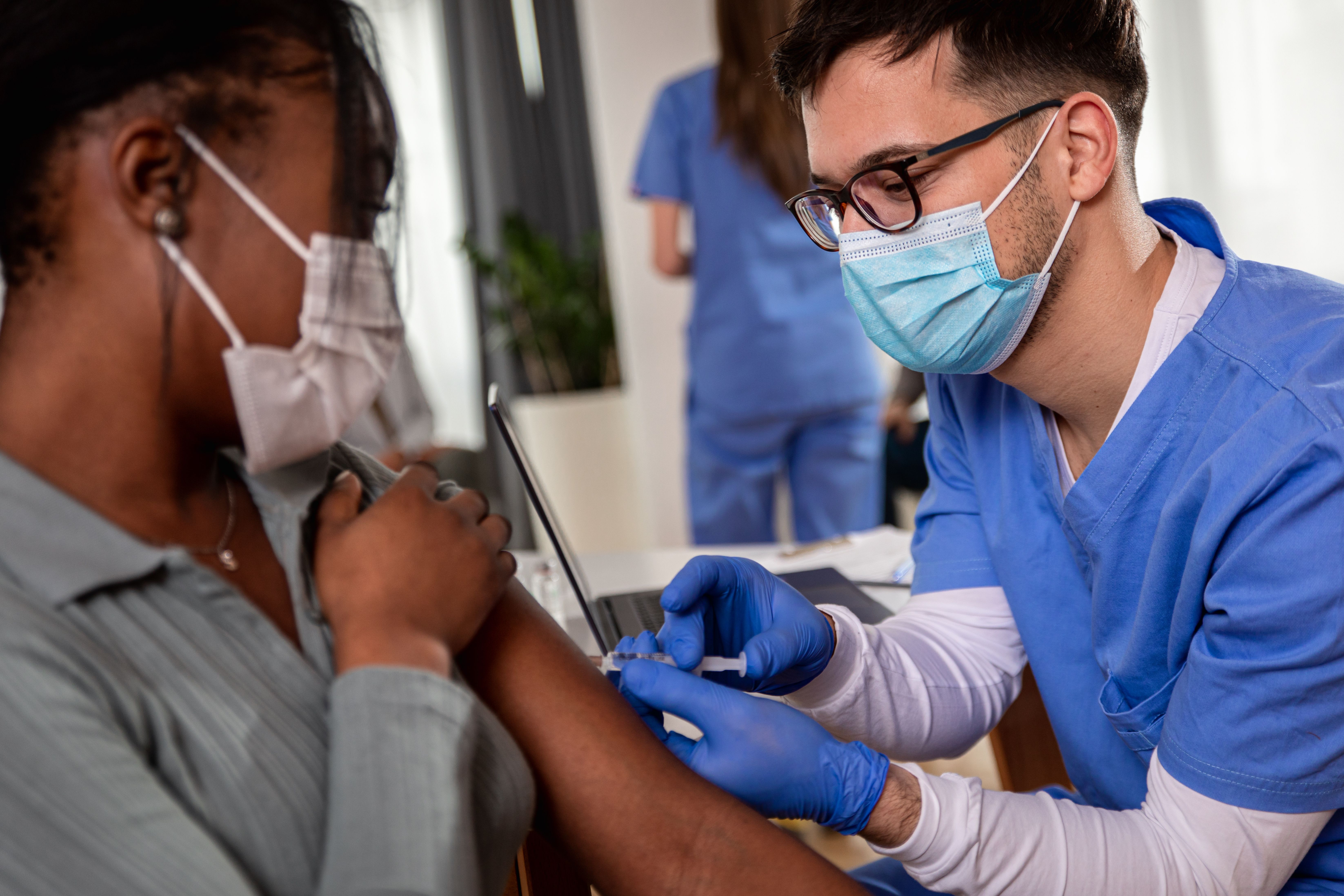 Male nurse with mask giving vaccine to patient in clinic. | Zoran Zeremski - stock.adobe.com