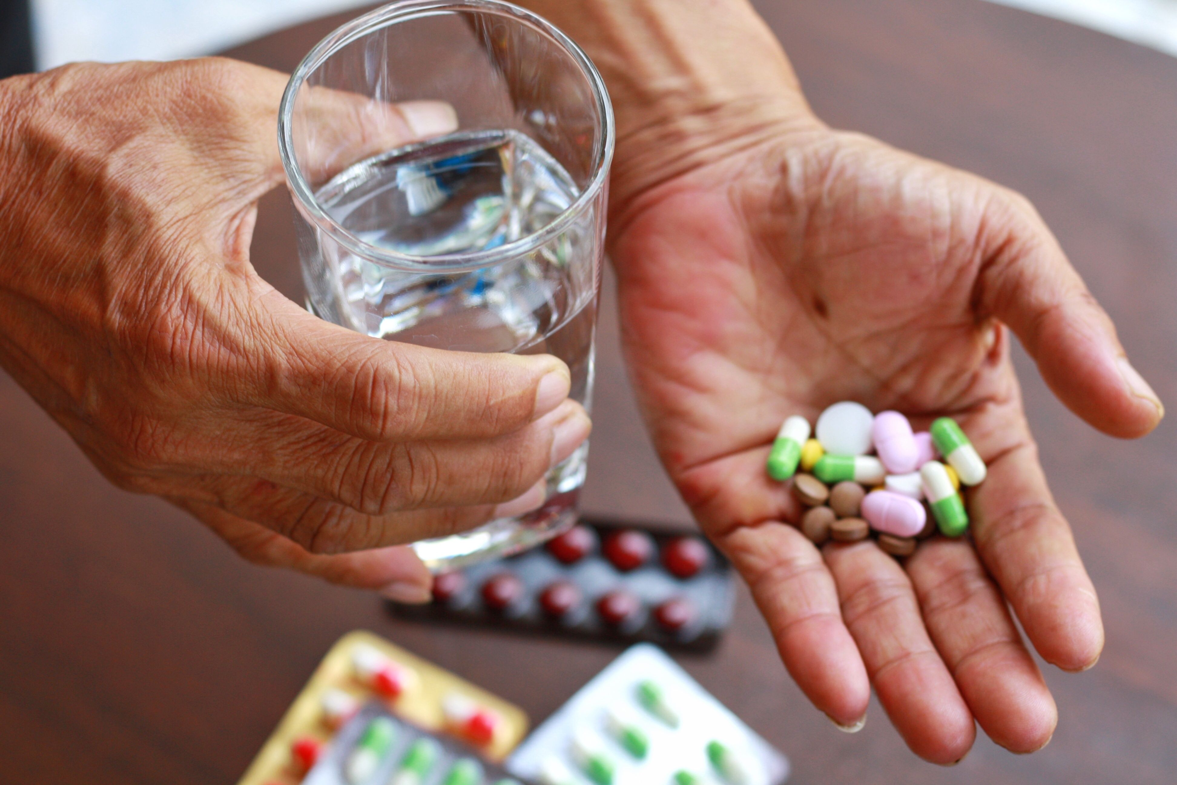 Older adult holding several pills and glass of water | Image credit: Kotchakorn – stock.adobe.com