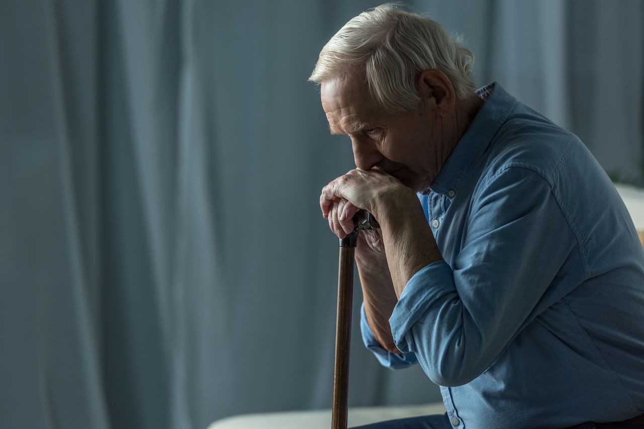 Senior sad man leans on a cane while sitting on sofa: © LIGHTFIELD STUDIOS - stock.adobe.com