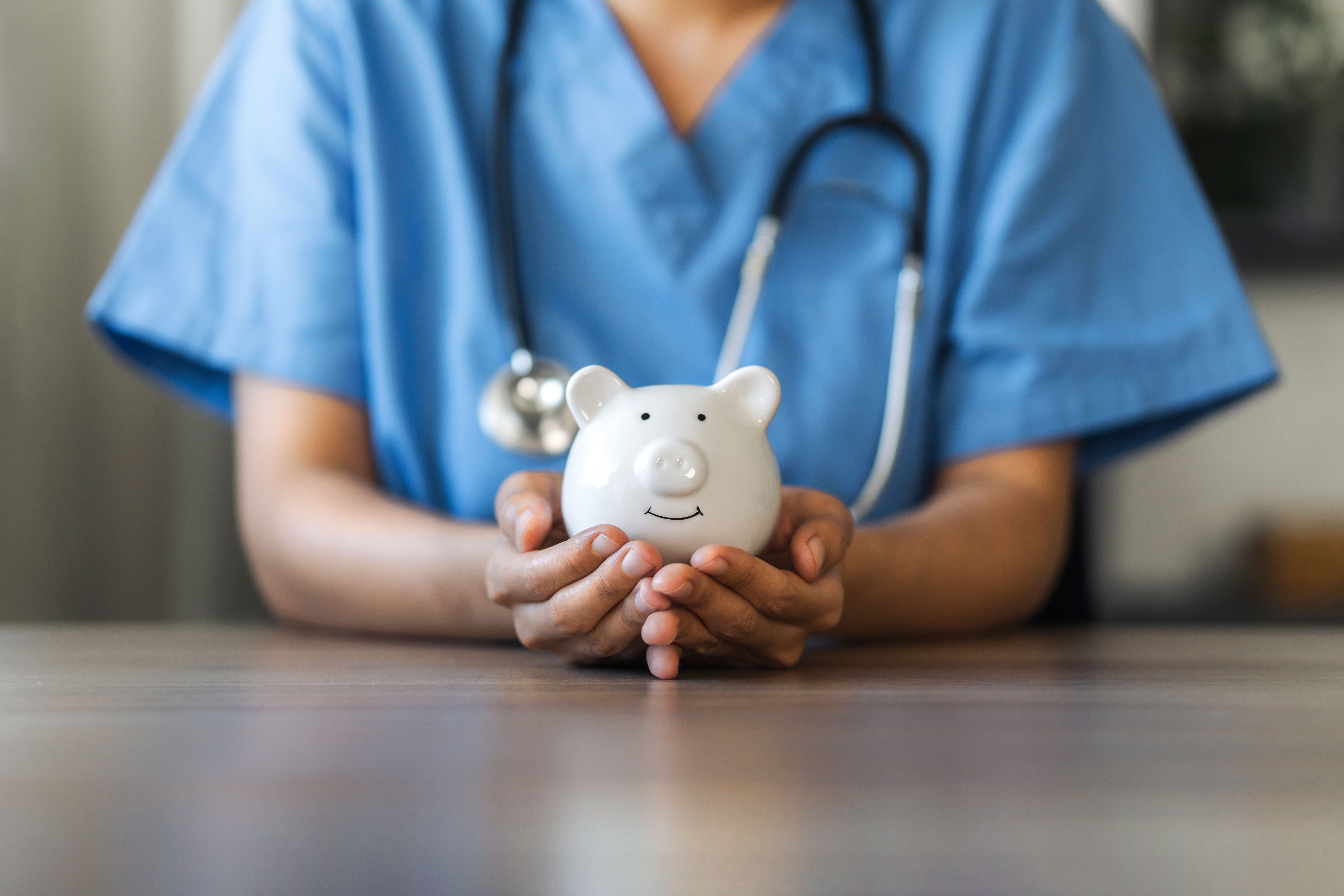 Clinician holding piggy bank | Image Credit: Dee Karen - stock.adobe.com