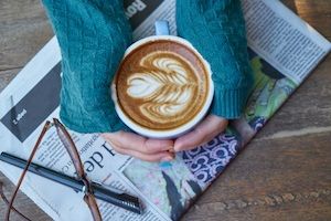 a person's hands are wrapped around a cup of coffee on top of a newspaper