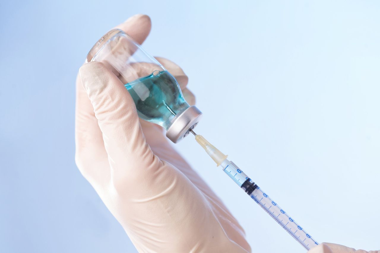 individual syringing vaccine from a vial into a needle 